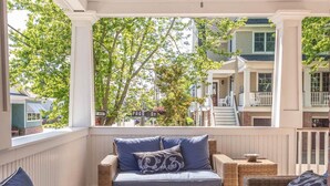 A covered porch with wicker furniture, a ceiling fan, and a view of a street and buildings. - CORNER BEACH HOUSE - COTTAGE (Cape May)
