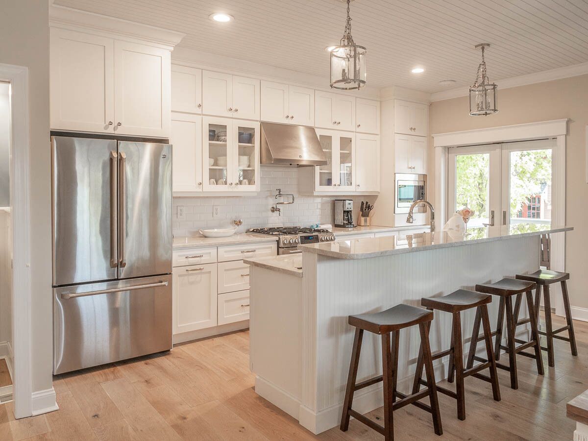 A modern kitchen with white cabinetry, stainless steel appliances, and a central island with bar stools.