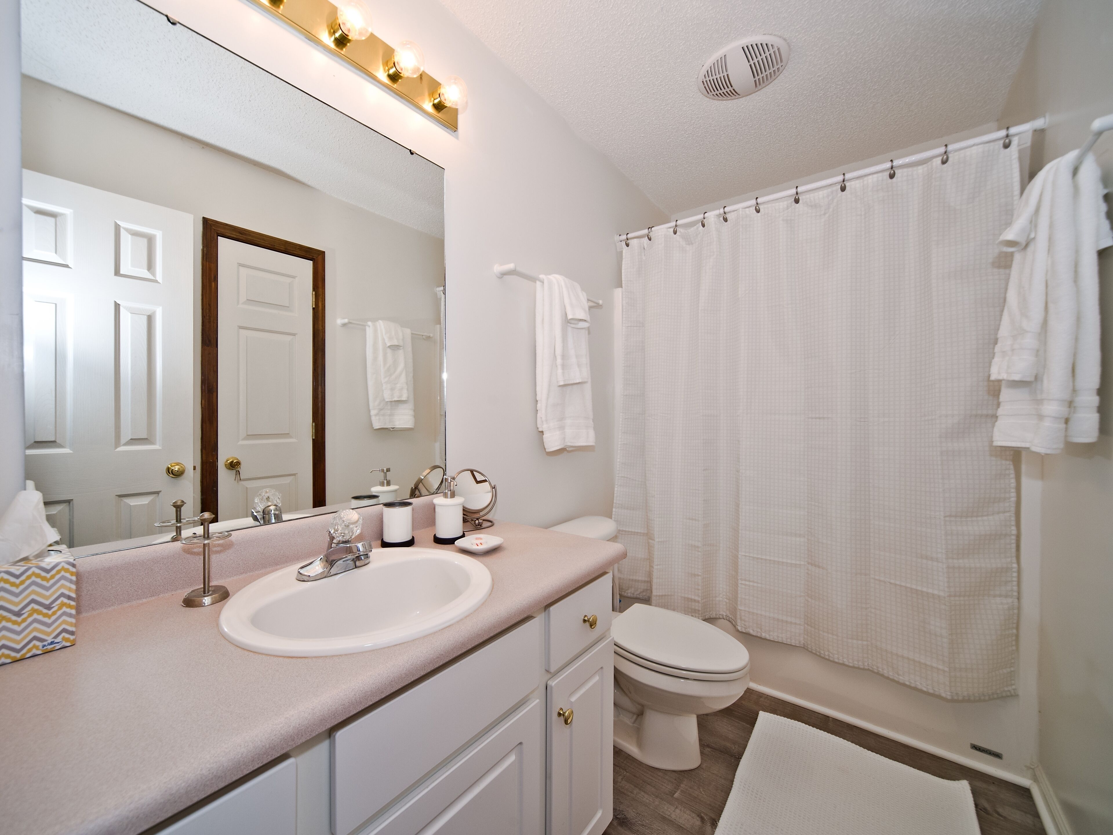 A bathroom with a white sink, vanity, and toilet. There is a shower curtain and a towel rack.
