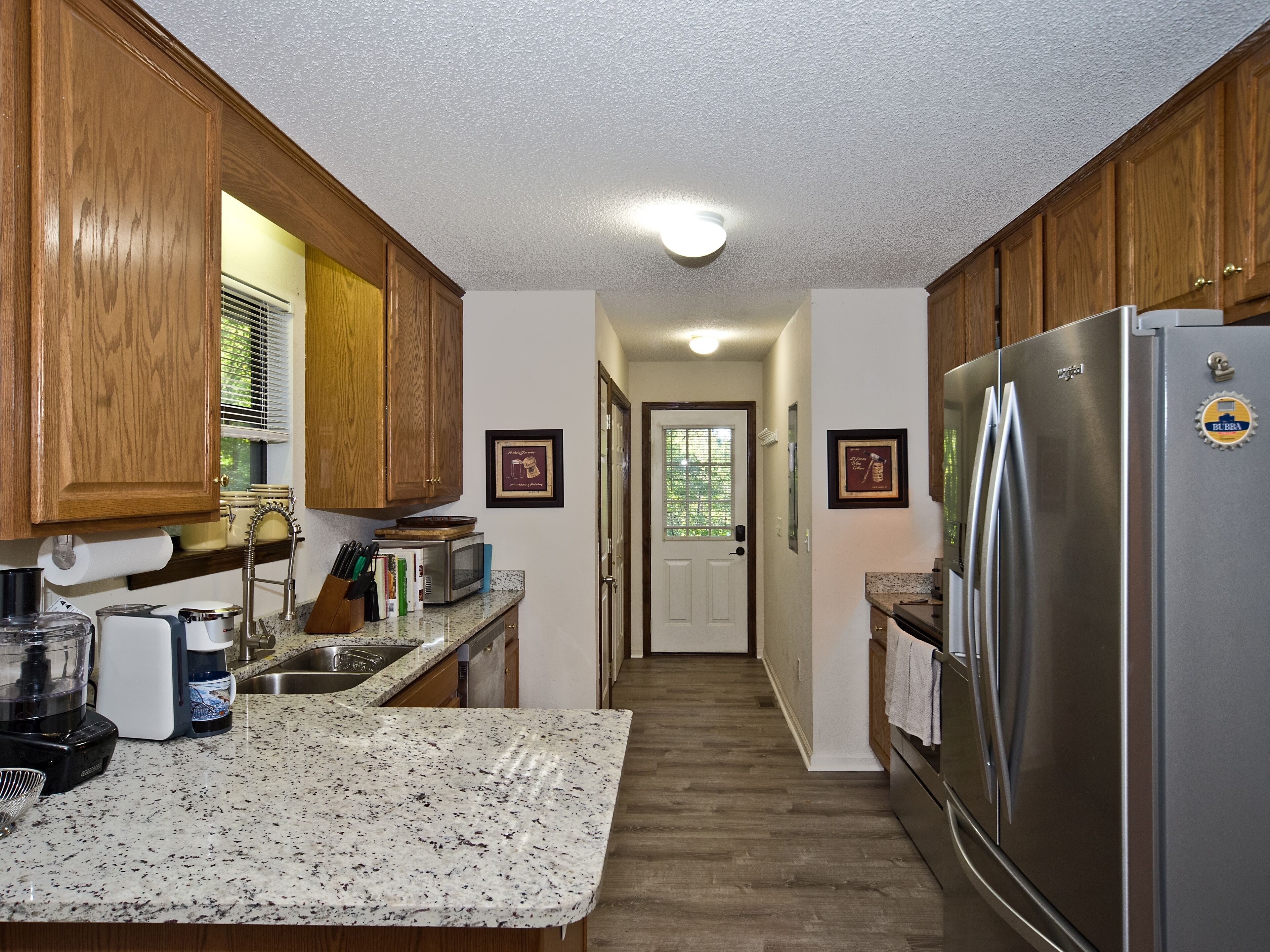A kitchen with wooden cabinets, a stainless steel refrigerator, granite countertops, and a microwave.