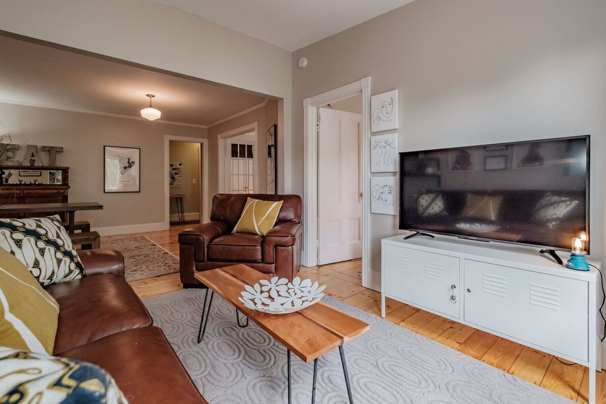 Een woonkamer met een bruine leren bank, een houten salontafel, een witte tv-meubel en een grote flatscreen televisie.