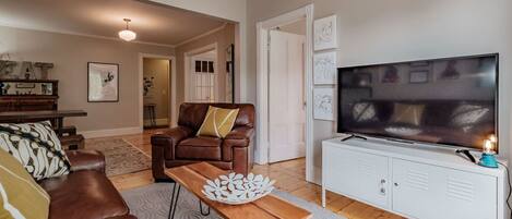 Een woonkamer met een bruine leren bank, een houten salontafel, een witte tv-meubel en een grote flatscreen televisie.