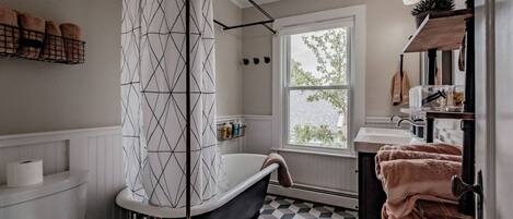 Une salle de bain avec une baignoire noire, des toilettes blanches, un carrelage à carreaux, une fenêtre avec vue et des serviettes rangées sur un porte-serviettes.
