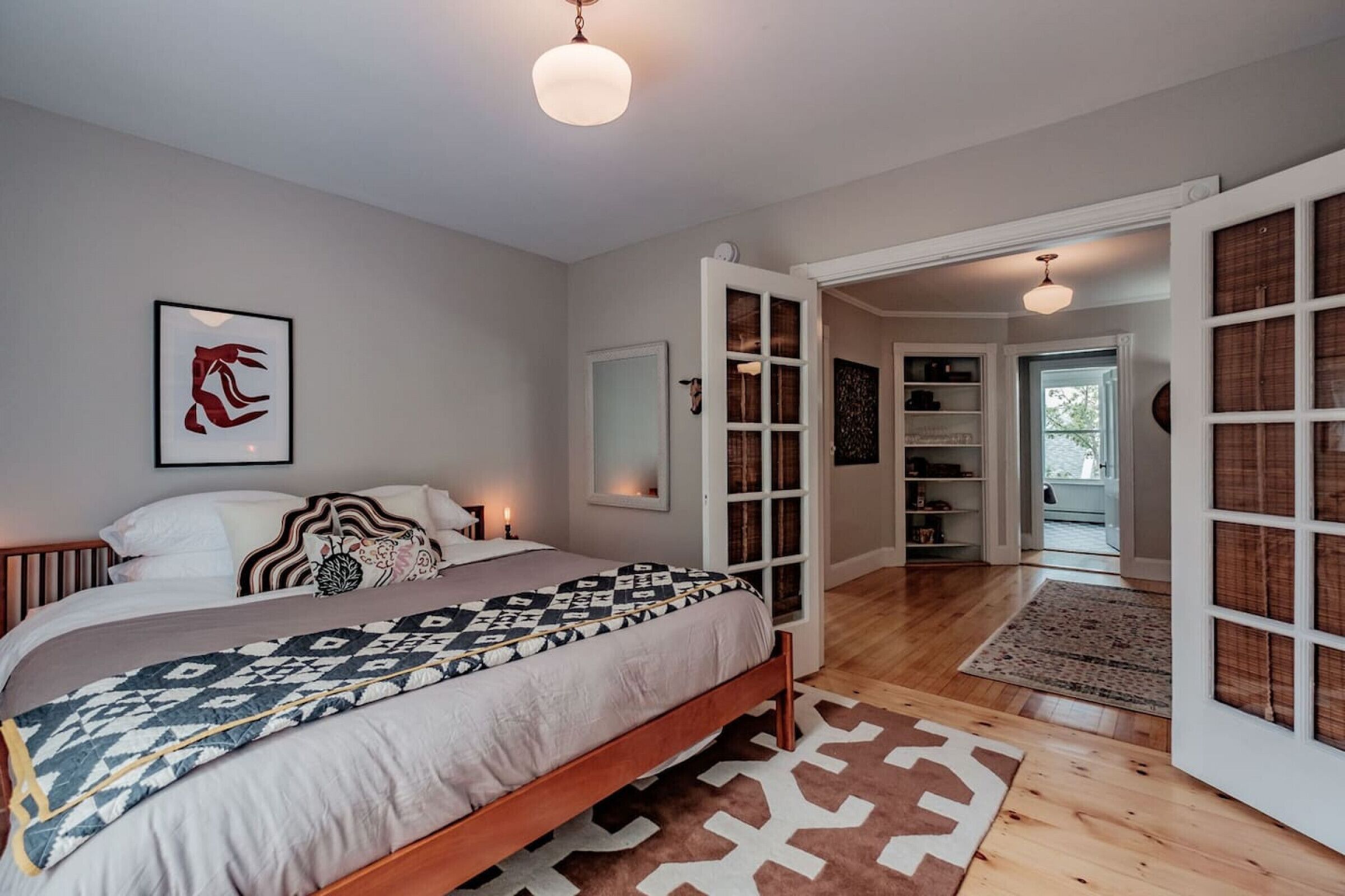 A bedroom with a bed, bedside tables, a mirror, and a door leading to another room.