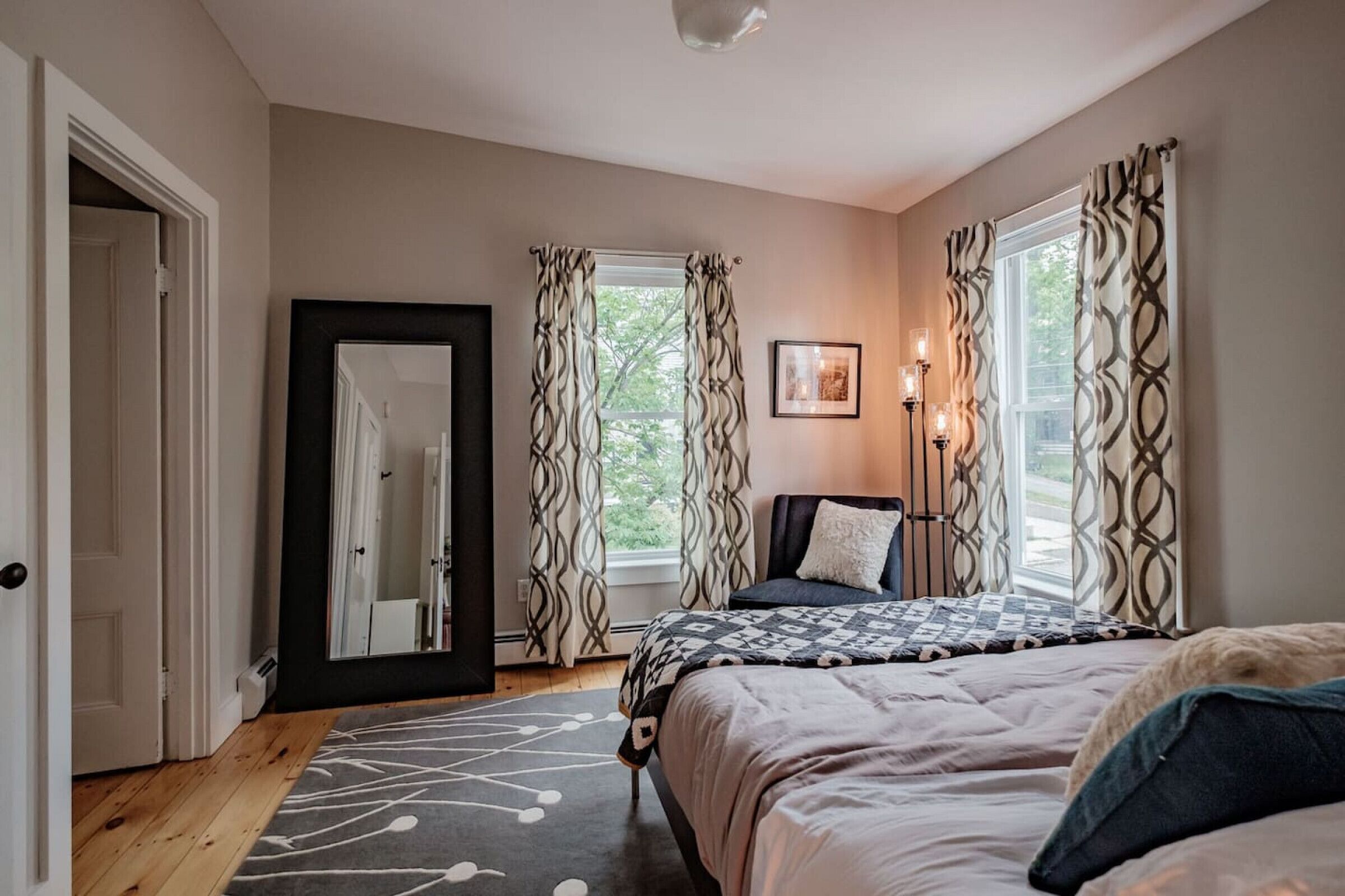 Une chambre à coucher avec un lit, une table de chevet avec une lampe, un miroir et une fenêtre avec des rideaux.
