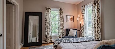 Une chambre à coucher avec un lit, une table de chevet avec une lampe, un miroir et une fenêtre avec des rideaux.