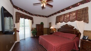 Une chambre avec un grand lit, un plancher en bois, un ventilateur de plafond et un téléviseur placé à gauche.