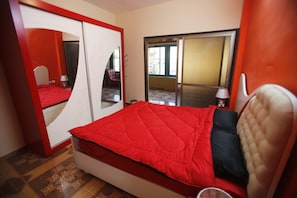 Un dormitorio con una colcha roja, un armario blanco y un espejo grande.