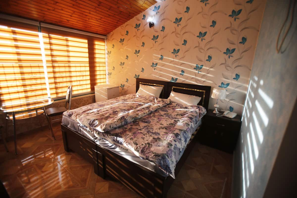 Quarto com teto de madeira, cama com roupa de cama floral, mesa de cabeceira com abajur e uma cadeira.