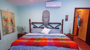 A bedroom with a bed, a wall-mounted air conditioner, a dreamcatcher, and a painting.
