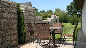 An outdoor patio with wicker furniture, a stone wall, and a grassy lawn. - Modern, quiet vacation apartment (30 m²) with separate entrance near the beach  (Seebad Ahlbeck)