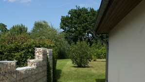 A paved pathway leading to a building with a stone wall on one side and a grassy area with a tree and bushes on the other. - Modern, quiet vacation apartment (30 m²) with separate entrance near the beach  (Seebad Ahlbeck)