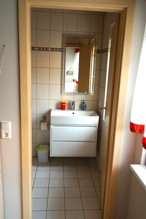 Une petite salle de bain avec un lavabo blanc, un miroir et un sol carrelé.