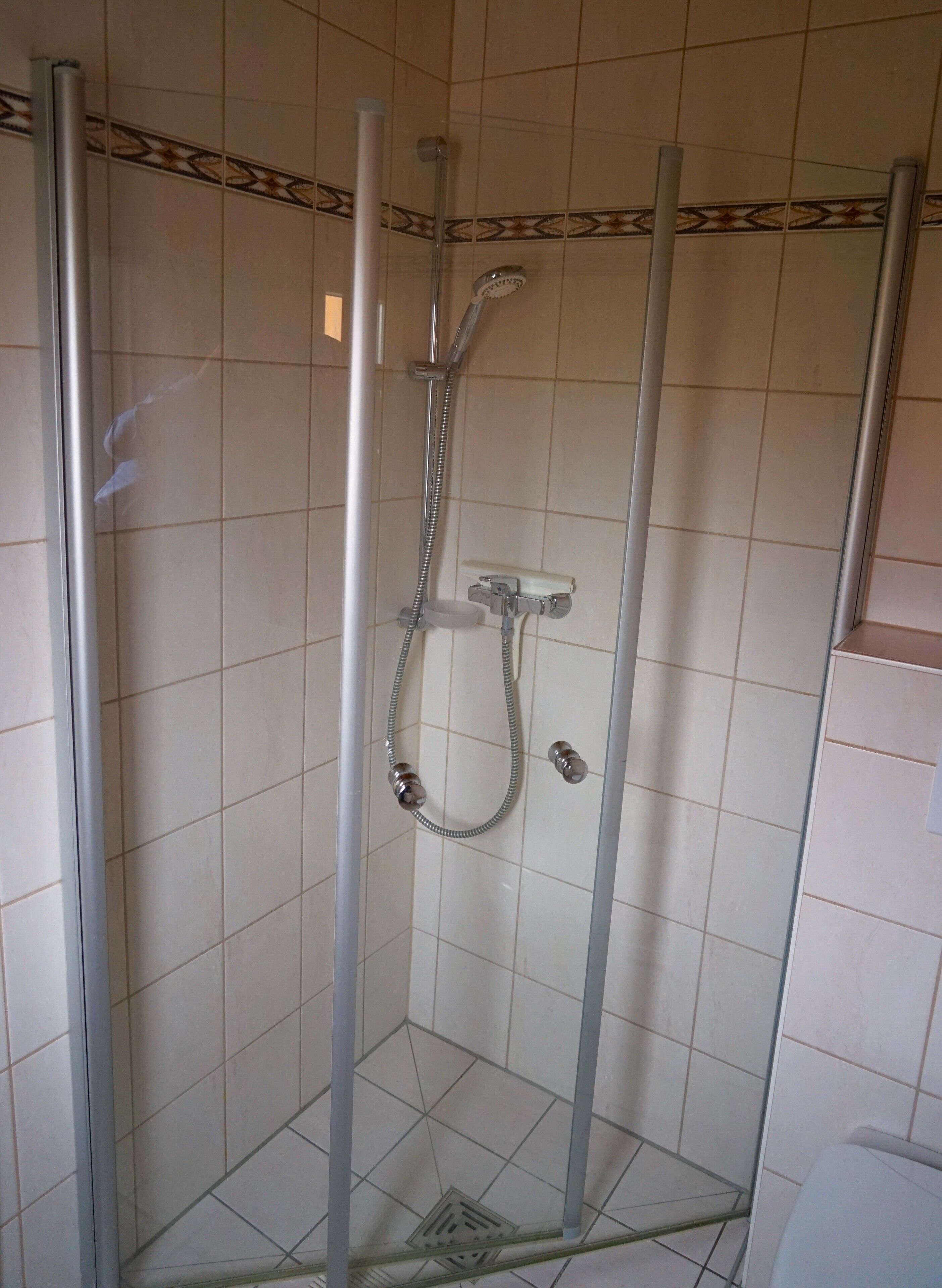 Een douchecabine met glazen wanden, een handdouche en een wandmengkraan.