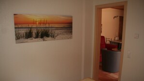 A bedroom with a bed, a painting of a sunset, and a view of a bathroom through an open door. - Modern, quiet vacation apartment (30 m²) with separate entrance near the beach  (Seebad Ahlbeck)