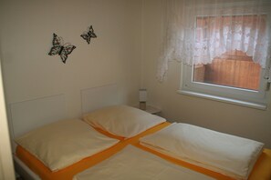 Une chambre à coucher avec un lit, deux oreillers, une table de chevet, une lampe et une fenêtre avec un rideau.