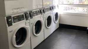 A laundry room with multiple washing machines and dryers, a tiled floor, and a window providing natural light. - 307-Centrally Located Studio Apt. in San Jose City (San Jose)