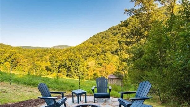 Ein Sitzbereich im Freien mit Adirondack-Stühlen und einem Feuerkorb, umgeben von einer Steinterrasse und üppiger Grünfläche.