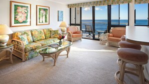 Ein Wohnzimmer mit einer Couch, Sesseln, einem Glastisch und Meerblick.