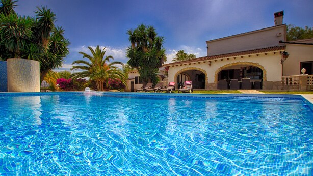 Una piscina con agua azul cristalina, rodeada de palmeras y un edificio con arcos.