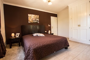 A bedroom with a large bed, dark walls, a ceiling light, a nightstand, a lamp, and a door. - Luxury villa with tennis court, guest house, pr. Pool, climate, playground, wellness, BBQ (Denia, Alicante)