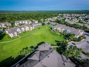 An aerial view of a residential area with multiple apartment buildings, green lawns, and a clear sky.