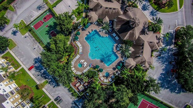 Vista aerea di un resort con piscina centrale, campi da tennis e area verde con palme.
