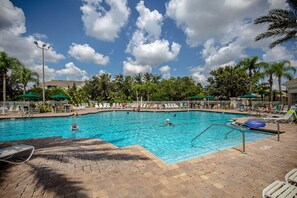 A swimming pool with lounge chairs and umbrellas, surrounded by palm trees and a clear sky.