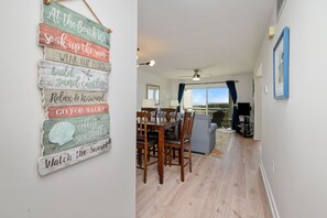 Ein Essbereich mit Holztisch und -stühlen, Blick ins Freie und einer Wand mit einem Strand-Schild.