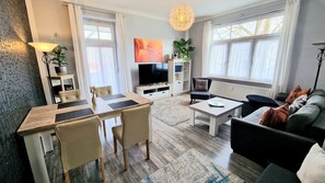 A modern living room with a dining area, a sofa set, a TV, and a decorative plant.
