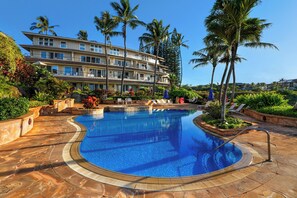 A hotel with a swimming pool, palm trees, and a multi-story building.