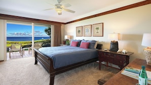 A hotel room with a bed, a desk, a chair, a lamp, and a view of the ocean. - Whalers Cove Unit #113 - Spectacular and Secluded Oceanfront Condo with Pool! (Koloa)