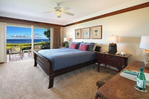 A hotel room with a bed, a desk, a chair, a lamp, and a view of the ocean.