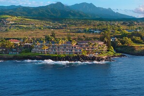 Un hôtel situé sur la côte, composé de plusieurs bâtiments, avec un rivage rocheux et un paysage montagneux en arrière-plan.