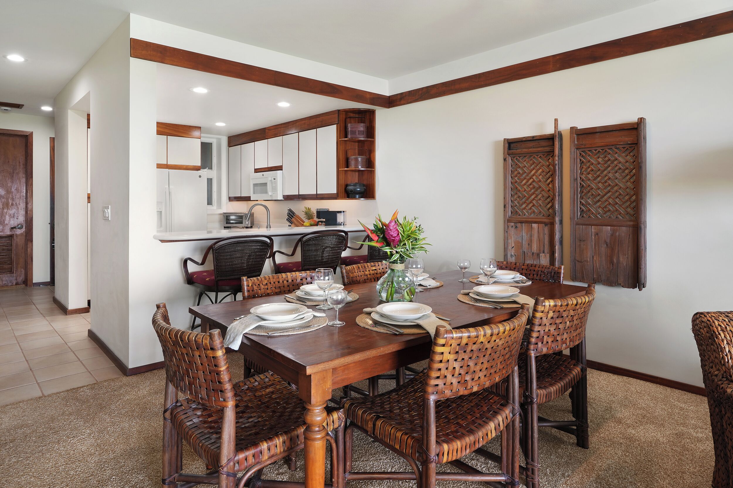 A dining area with a wooden table set for six, surrounded by wicker chairs.