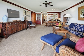 A spacious living room with a high ceiling, a dining area, and a kitchen in the background.