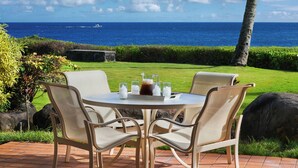 An outdoor seating area with a table and chairs, overlooking a body of water. - Whalers Cove Unit #113 - Spectacular and Secluded Oceanfront Condo with Pool! (Koloa)