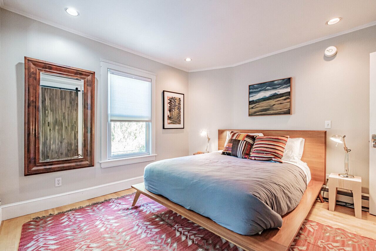 Une chambre à coucher avec un lit, une fenêtre, un tableau accroché au mur et une table de chevet.
