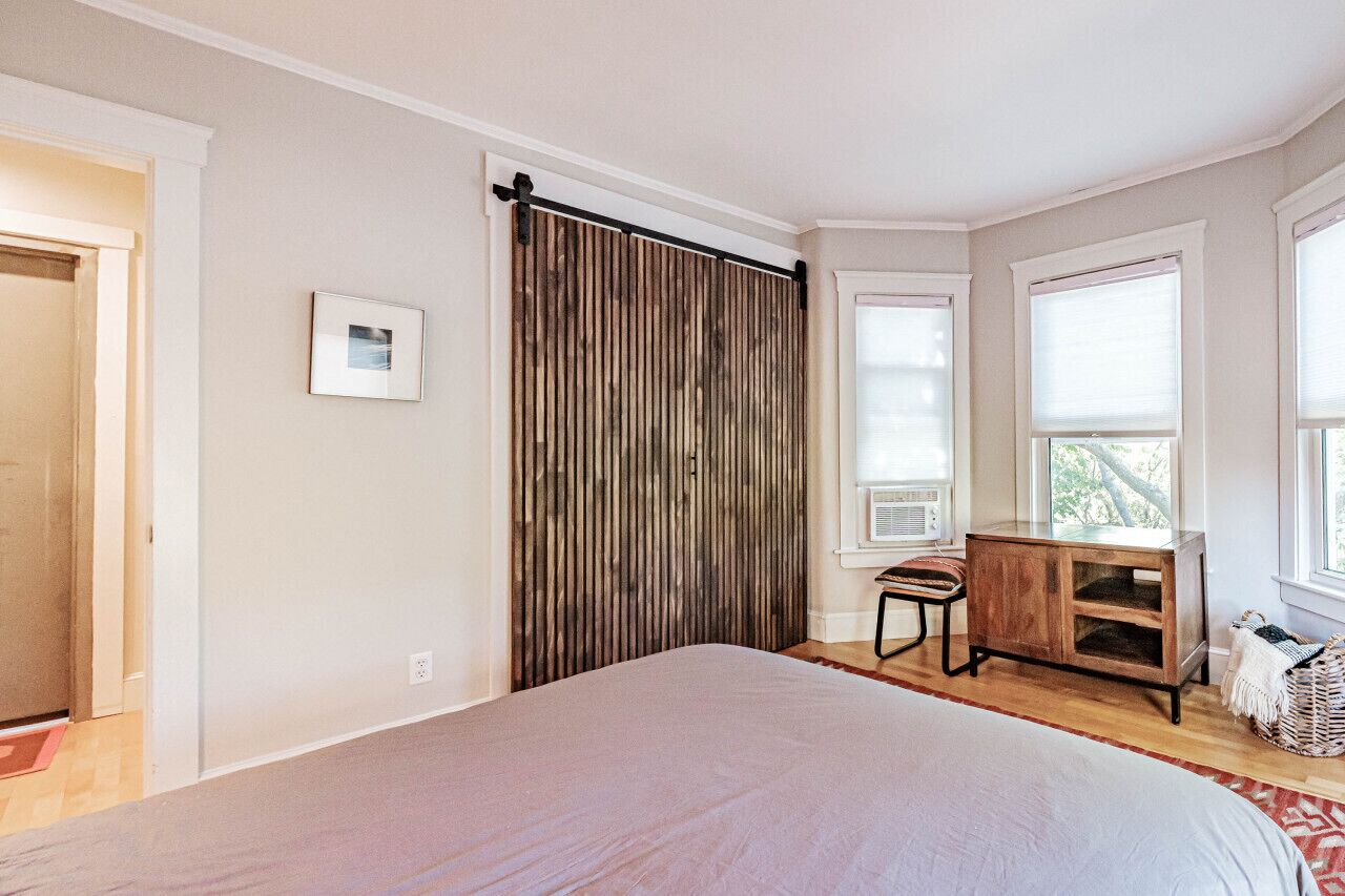 Ein Schlafzimmer mit einem großen Bett, einem Holzschrank, einer kleinen Holzkommode und einem Fenster mit Jalousien.