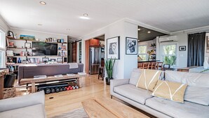 Una sala moderna con un televisor de pantalla plana grande, un sofá gris, una mesa de centro de madera y un comedor con una cocina al fondo.