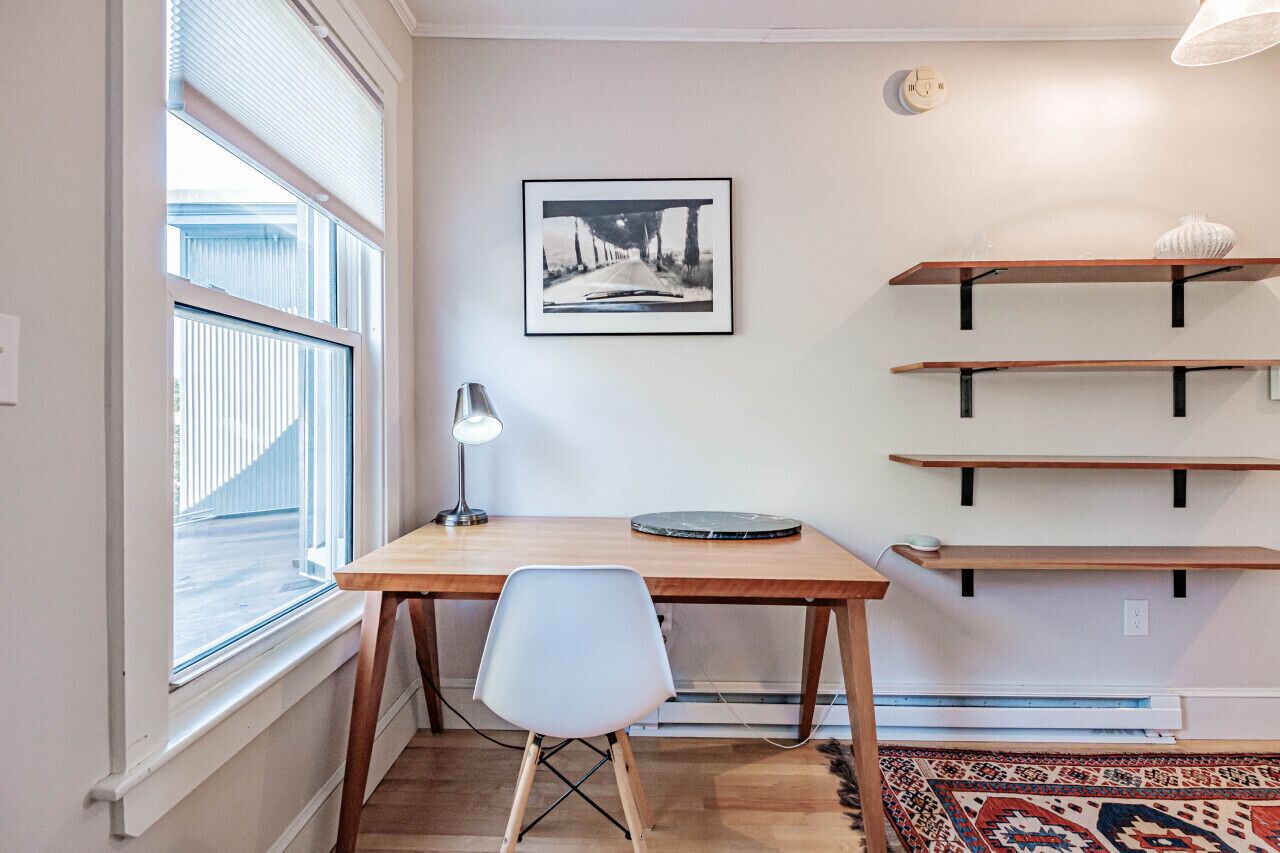 Ein Zimmer mit Schreibtisch aus Holz, einem weißen Stuhl, einem gerahmten Bild an der Wand und eingebauten Regalen.