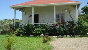 Ein einstöckiges Haus mit rotem Dach, einer überdachten Veranda und einem Garten mit verschiedenen Pflanzen und Blumen.