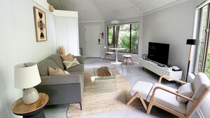 A modern living room with a sofa, coffee table, TV, and a dining area with a table and chairs. - Newly renovated cottage in Sea Pines. Private setting with a short walk to beach (Hilton Head Island)