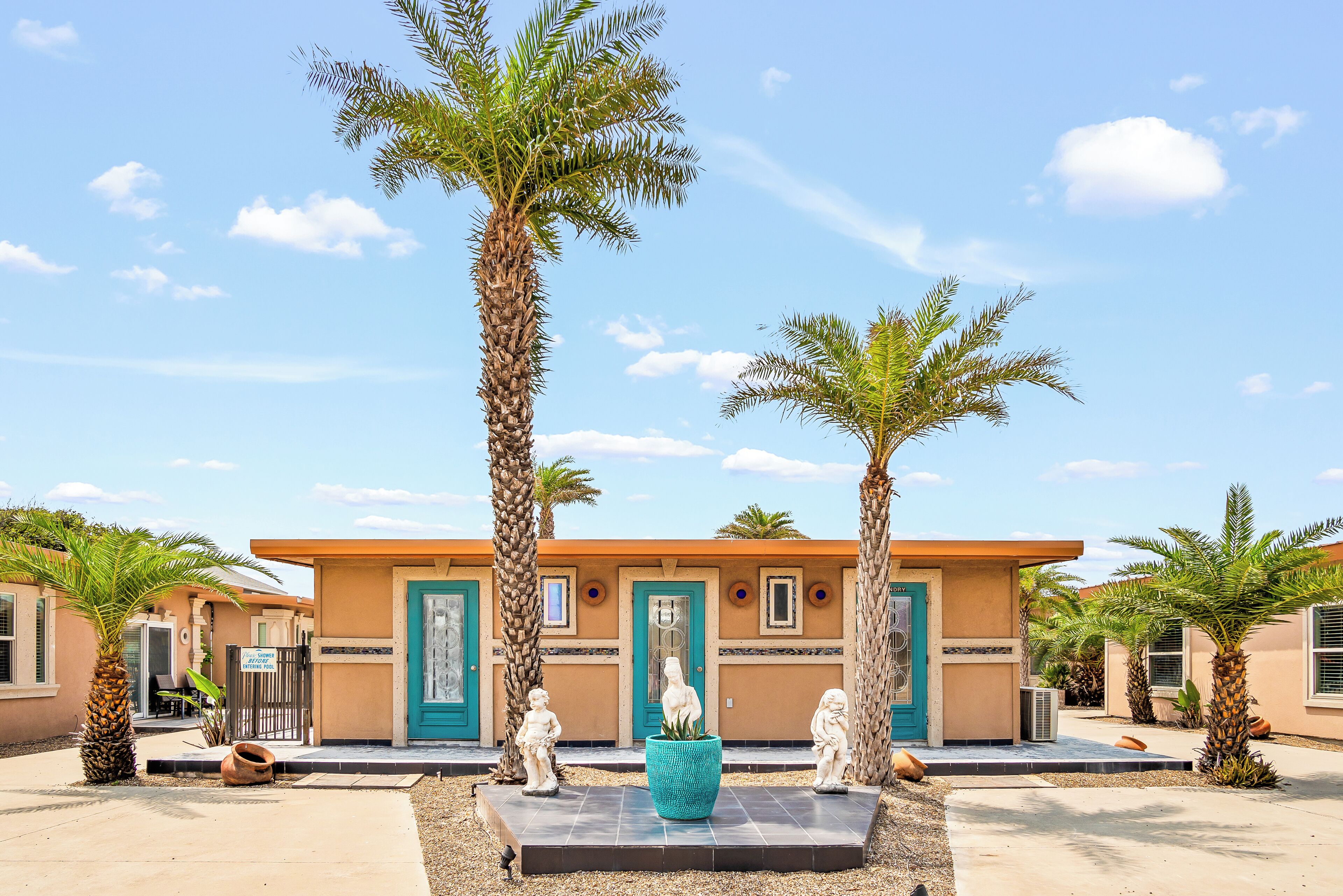 A building with a beige facade, turquoise accents, and palm trees.