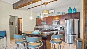 Una cocina moderna con una isla central, taburetes de bar, electrodomésticos de acero inoxidable y armarios de madera.