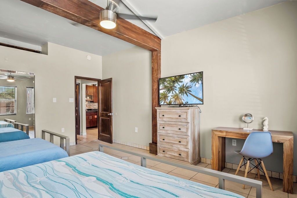 Habitación de hotel con dos camas, un escritorio de madera, una silla, un aparador y un cuadro de palmeras.