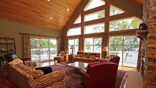 A spacious living room with a high ceiling, large windows, and a stone fireplace. - PRIVATE Luxury Lake Home with 5+ BR and Gourmet Kitchen-22 Foot Pontoon Included (Alexandria)