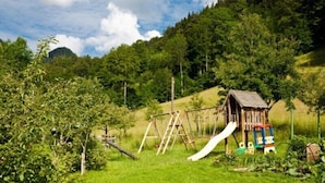 Ein Spielplatz mit Rutsche und Schaukeln, umgeben von üppigem Grün und einer sanften Hügelkulisse.