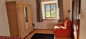 Ein Zimmer mit Holzschrank, einem Vorhangfenster, einem roten Sofa und einem schwarzen Teppich.