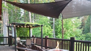 Una terraza al aire libre con mobiliario de madera, una chimenea y una pérgola con luces colgantes.